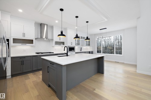 Kitchen featuring two tone color scheme, light wood finished floors, a kitchen island with sink, light stone counters, and decorative backsplash - 718 Elderberry Close Nw, Edmonton, AB - Indoor Photo Showing Kitchen With Upgraded Kitchen
