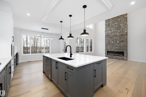 Kitchen featuring a fireplace, two tone cabinetry, light wood-type flooring, pendant lighting, and a center island with sink - 718 Elderberry Close Nw, Edmonton, AB - Indoor Photo Showing Kitchen With Double Sink With Upgraded Kitchen