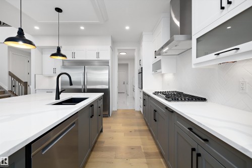 Kitchen featuring stainless steel appliances, light wood-type flooring, two tone color scheme, decorative light fixtures, and light stone counters - 718 Elderberry Close Nw, Edmonton, AB - Indoor Photo Showing Kitchen With Double Sink With Upgraded Kitchen
