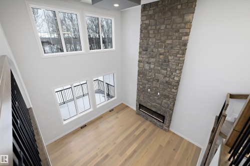 Unfurnished living room with a stone fireplace, light wood finished floors, a high ceiling, and recessed lighting - 718 Elderberry Close Nw, Edmonton, AB - Indoor Photo Showing Other Room
