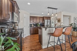 Kitchen with stainless steel appliances, a kitchen bar, hanging light fixtures, dark wood-style flooring, and a textured ceiling - 