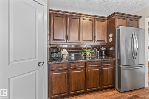 Kitchen with freestanding refrigerator, wood finished floors, a textured ceiling, backsplash, and dark stone counters - 10415 94 Street, Morinville, AB - Indoor Photo Showing Kitchen