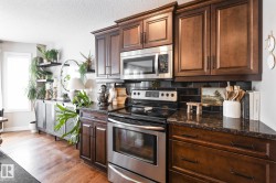 Kitchen featuring stainless steel appliances, tasteful backsplash, light wood-style floors, dark wood finish cabinets, and a textured ceiling - 