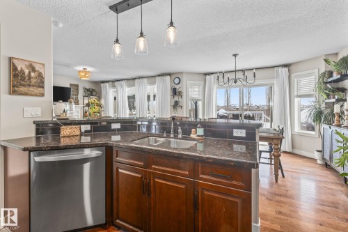 Kitchen with stainless steel dishwasher, dark stone countertops, a chandelier, a textured ceiling, and a peninsula - 10415 94 Street, Morinville, AB - Indoor Photo Showing Kitchen With Double Sink