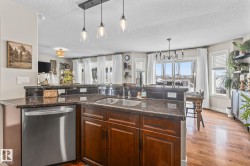 Kitchen with stainless steel dishwasher, dark stone countertops, a chandelier, a textured ceiling, and a peninsula - 