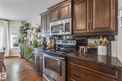 Kitchen featuring stainless steel appliances, dark wood finish cabinets, tasteful backsplash, dark stone counters, and dark wood-style floors - 