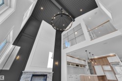 Kitchen view of hanging light fixtures, a stone fireplace, white cabinetry, open shelves, and light stone counters - 