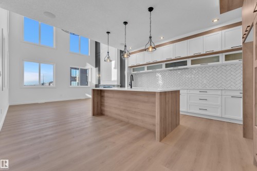 Two tone kitchen with dual tone cabinets, decorative light fixtures, an island with sink, light wood-style flooring, and decorative backsplash - 95 Eldridge Point(E), St. Albert, AB - Indoor Photo Showing Kitchen