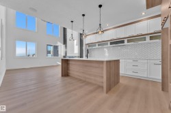 Two tone kitchen with dual tone cabinets, decorative light fixtures, an island with sink, light wood-style flooring, and decorative backsplash - 