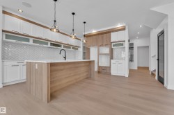 Dual tone kitchen featuring decorative light fixtures, tasteful backsplash, dual tone cabinets, light stone counters, and a center island with sink - 