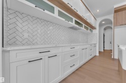 Kitchen with white cabinetry, glass insert cabinets, light stone countertops, light wood-style flooring, and arched walkways - 