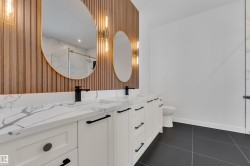 Full bath featuring wallpapered walls, double vanity, a marble finish shower, and dark tile patterned floors - 
