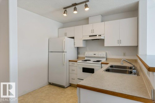 Kitchen with white appliances, light countertops, track lighting, light floors, and white cabinetry - 403 14708 50 Street, Edmonton, AB - Indoor Photo Showing Kitchen With Double Sink