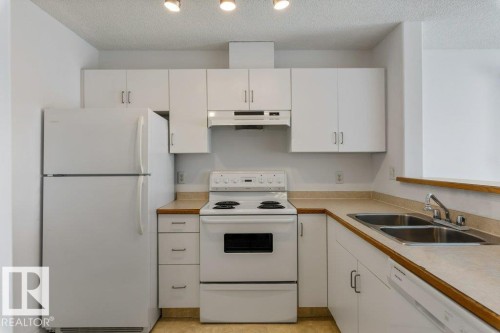 Kitchen featuring white appliances, light countertops, white cabinetry, and a textured ceiling - 403 14708 50 Street, Edmonton, AB - Indoor Photo Showing Kitchen With Double Sink