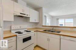 Kitchen with white appliances, light countertops, white cabinetry, and a textured ceiling - 
