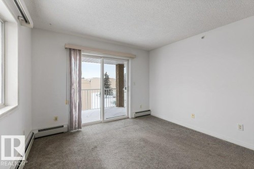 Carpeted empty room featuring a textured ceiling and a baseboard heating unit - 403 14708 50 Street, Edmonton, AB - Indoor Photo Showing Other Room
