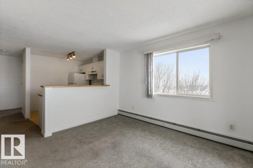 Unfurnished living room with a baseboard radiator, light carpet, and a textured ceiling - 403 14708 50 Street, Edmonton, AB - Indoor Photo Showing Other Room