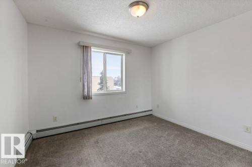 Carpeted empty room with a baseboard radiator and a textured ceiling - 403 14708 50 Street, Edmonton, AB - Indoor Photo Showing Other Room
