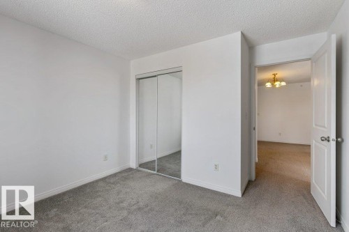 Unfurnished bedroom with a textured ceiling, light carpet, a closet, and a chandelier - 403 14708 50 Street, Edmonton, AB - Indoor Photo Showing Other Room
