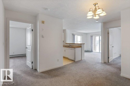 Unfurnished room with light carpet, suspended lighting, a textured ceiling, and a baseboard heating unit - 403 14708 50 Street, Edmonton, AB - Indoor Photo Showing Other Room