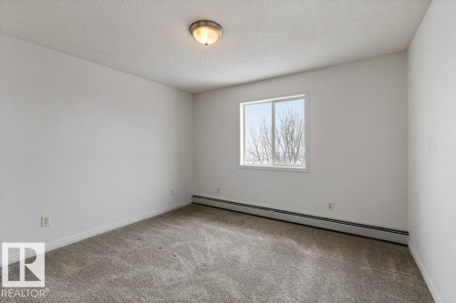 Empty room featuring baseboard heating, a textured ceiling, and light colored carpet - 403 14708 50 Street, Edmonton, AB - Indoor Photo Showing Other Room
