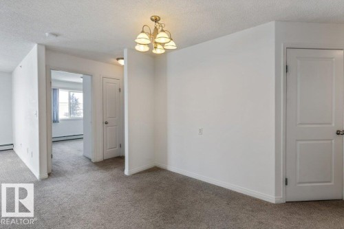 Carpeted spare room featuring a textured ceiling, suspended lighting, and a baseboard radiator - 403 14708 50 Street, Edmonton, AB - Indoor Photo Showing Other Room