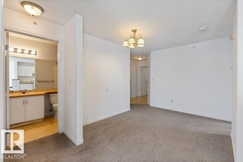 Empty room with light carpet, a textured ceiling, and hanging lights - 403 14708 50 Street, Edmonton, AB - Indoor