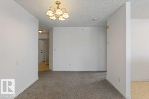 Empty room with a chandelier, light carpet, and a textured ceiling - 403 14708 50 Street, Edmonton, AB - Indoor Photo Showing Other Room