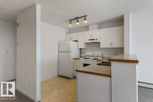 Kitchen with white appliances, light countertops, light floors, white cabinets, and rail lighting - 403 14708 50 Street, Edmonton, AB - Indoor Photo Showing Kitchen With Double Sink