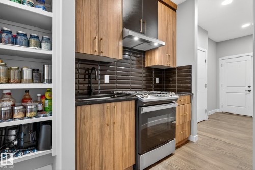 Kitchen featuring stainless steel range with gas stovetop, modern cabinets, tasteful backsplash, light wood-style floors, and dark stone counters - 1027 150 Avenue, Edmonton, AB - Indoor Photo Showing Other Room
