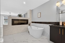 Full bath with vanity, light marble finish flooring, a freestanding tub, a glass covered fireplace, and tile walls - 