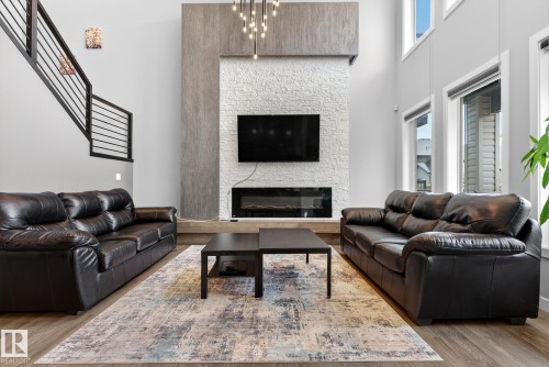 Living area featuring a glass covered fireplace, a high ceiling, light wood-style floors, and suspended lighting - 1027 150 Avenue, Edmonton, AB - Indoor Photo Showing Living Room With Fireplace