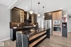 Kitchen with dark stone countertops, a kitchen island with sink, pendant lighting, stainless steel appliances, and open shelves - 