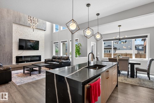 Kitchen featuring suspended lighting, open floor plan, a fireplace, a kitchen island with sink, and dark stone countertops - 1027 150 Avenue, Edmonton, AB - Indoor With Fireplace
