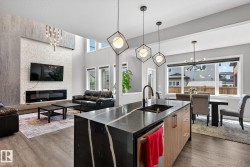 Kitchen featuring suspended lighting, open floor plan, a fireplace, a kitchen island with sink, and dark stone countertops - 