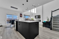 Kitchen with dark cabinetry, pendant lighting, an island with sink, light wood-type flooring, and a high ceiling - 