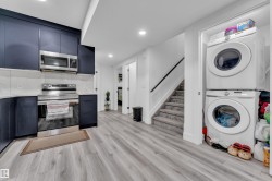 Kitchen with modern cabinets, stainless steel appliances, stacked washer / drying machine, light wood-style floors, and recessed lighting - 