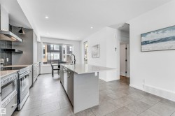 Kitchen with an island with sink, stainless steel appliances, open shelves, tasteful backsplash, and light stone counters - 