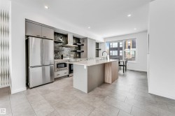 Kitchen featuring stainless steel appliances, an island with sink, modern cabinets, open shelves, and tasteful backsplash - 