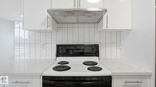 Kitchen view of white electric range, white cabinetry, range hood, and light stone countertops - 3419 143 Avenue Nw, Edmonton, AB - Indoor Photo Showing Kitchen