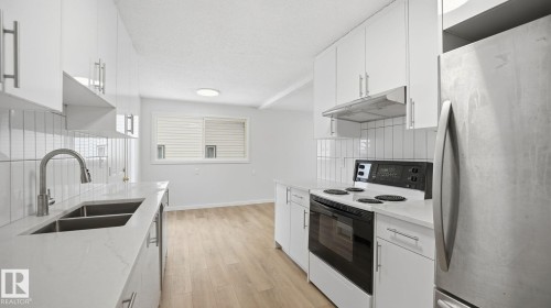 Kitchen with freestanding refrigerator, range with electric stovetop, white cabinetry, light wood-style flooring, and a textured ceiling - 3419 143 Avenue Nw, Edmonton, AB - Indoor Photo Showing Kitchen With Double Sink