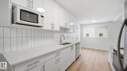 Kitchen with white microwave, white cabinetry, light wood-type flooring, fridge, and decorative backsplash - 