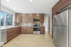 Kitchen featuring stainless steel appliances, modern cabinets, light stone countertops, recessed lighting, and decorative backsplash - 