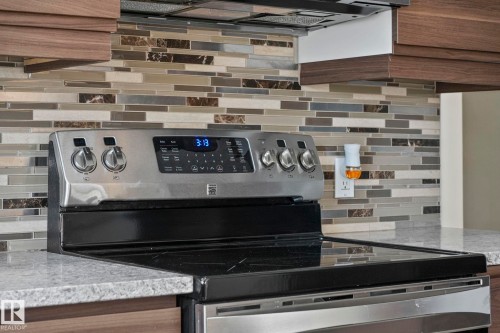 Kitchen view of stainless steel electric stove, tasteful backsplash, light stone countertops, and wood finish cabinets - 13911 117 Avenue, Edmonton, AB - Indoor Photo Showing Kitchen