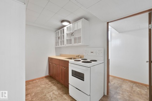 Kitchen featuring white range with electric stovetop, two tone cabinetry, light countertops, glass fronted cabinets, and stone finish flooring - 13911 117 Avenue, Edmonton, AB - Indoor Photo Showing Kitchen