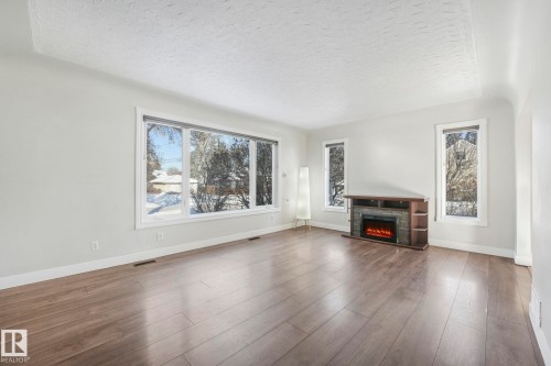 Unfurnished living room featuring a textured ceiling, a fireplace, and wood finished floors - 13911 117 Avenue, Edmonton, AB - Indoor Photo Showing Living Room With Fireplace