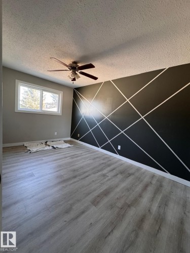 Spacious room featuring a contemporary accent wall with geometric pattern, wood-finish flooring, and a ceiling fan with integrated lighting - 2910 132A Avenue, Edmonton, AB - Indoor