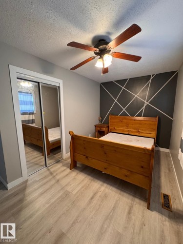 Light wood-finish flooring, mirrored closet doors, contemporary accent wall, and ceiling fan with integrated lighting - 2910 132A Avenue, Edmonton, AB - Indoor Photo Showing Bedroom