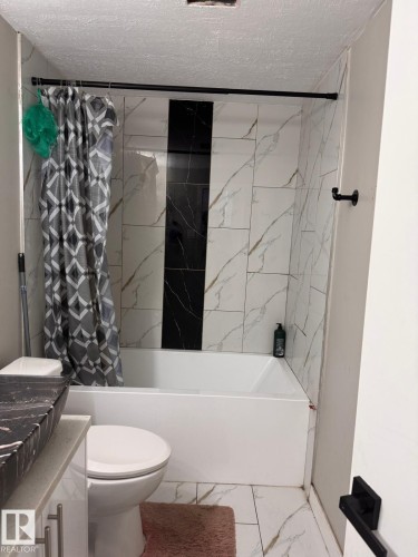 Full bathroom featuring a white bathtub, white and black marble-patterned wall tiling, and a black vessel sink with a light countertop - 2910 132A Avenue, Edmonton, AB - Indoor Photo Showing Bathroom