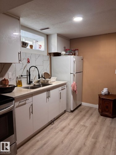 Kitchen featuring light wood-finish flooring, white cabinetry, a double basin sink with a black gooseneck faucet, light-toned countertops, and a white tile backsplash - 2910 132A Avenue, Edmonton, AB - Indoor Photo Showing Kitchen With Double Sink
